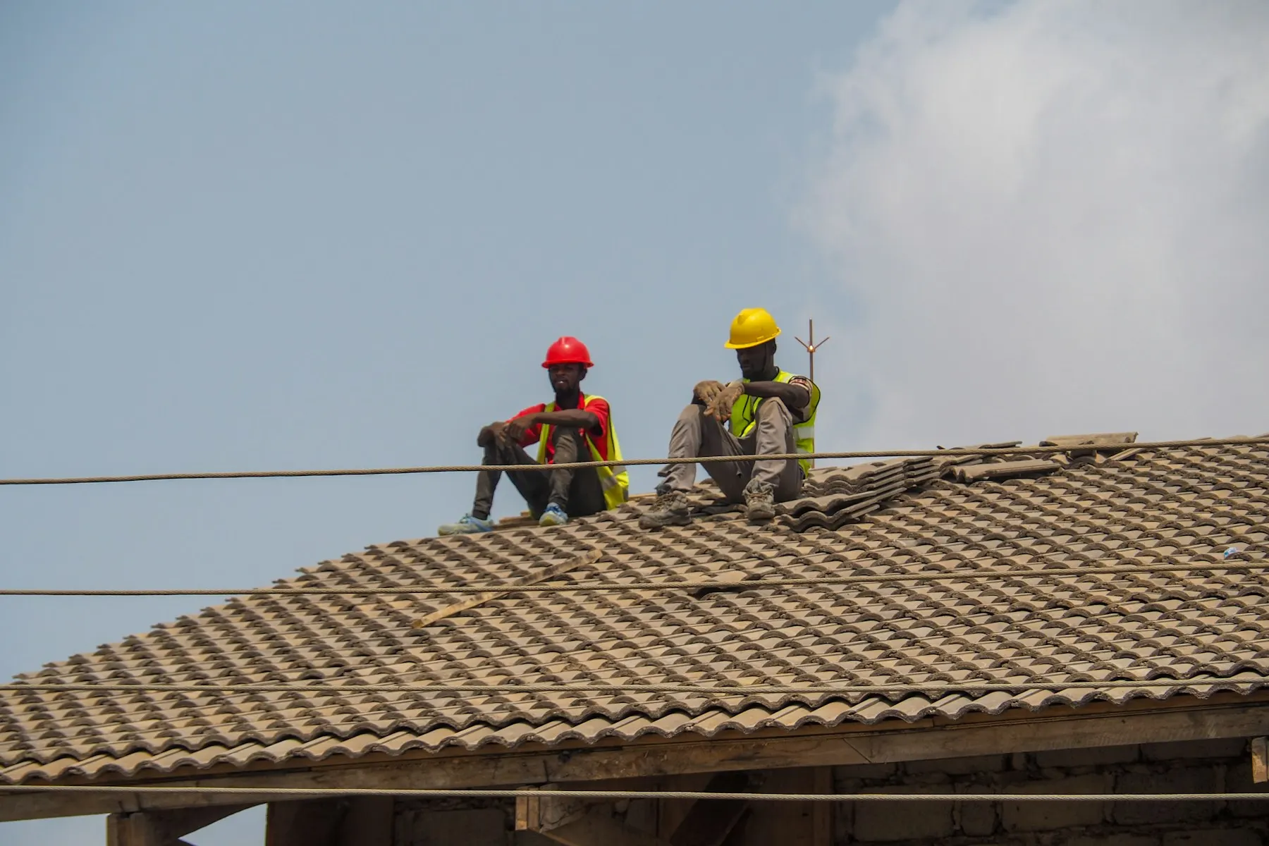 Two construction workers in hard hats resting on a tiled roof