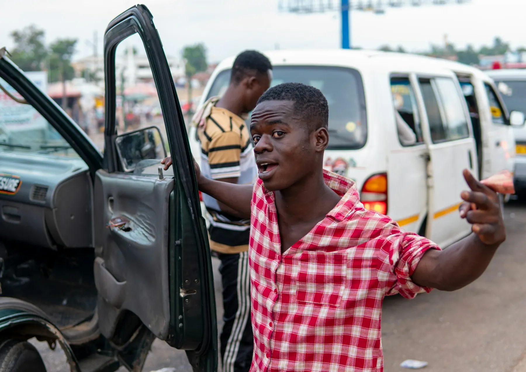 A young man leaning out of a minibus door on a busy road