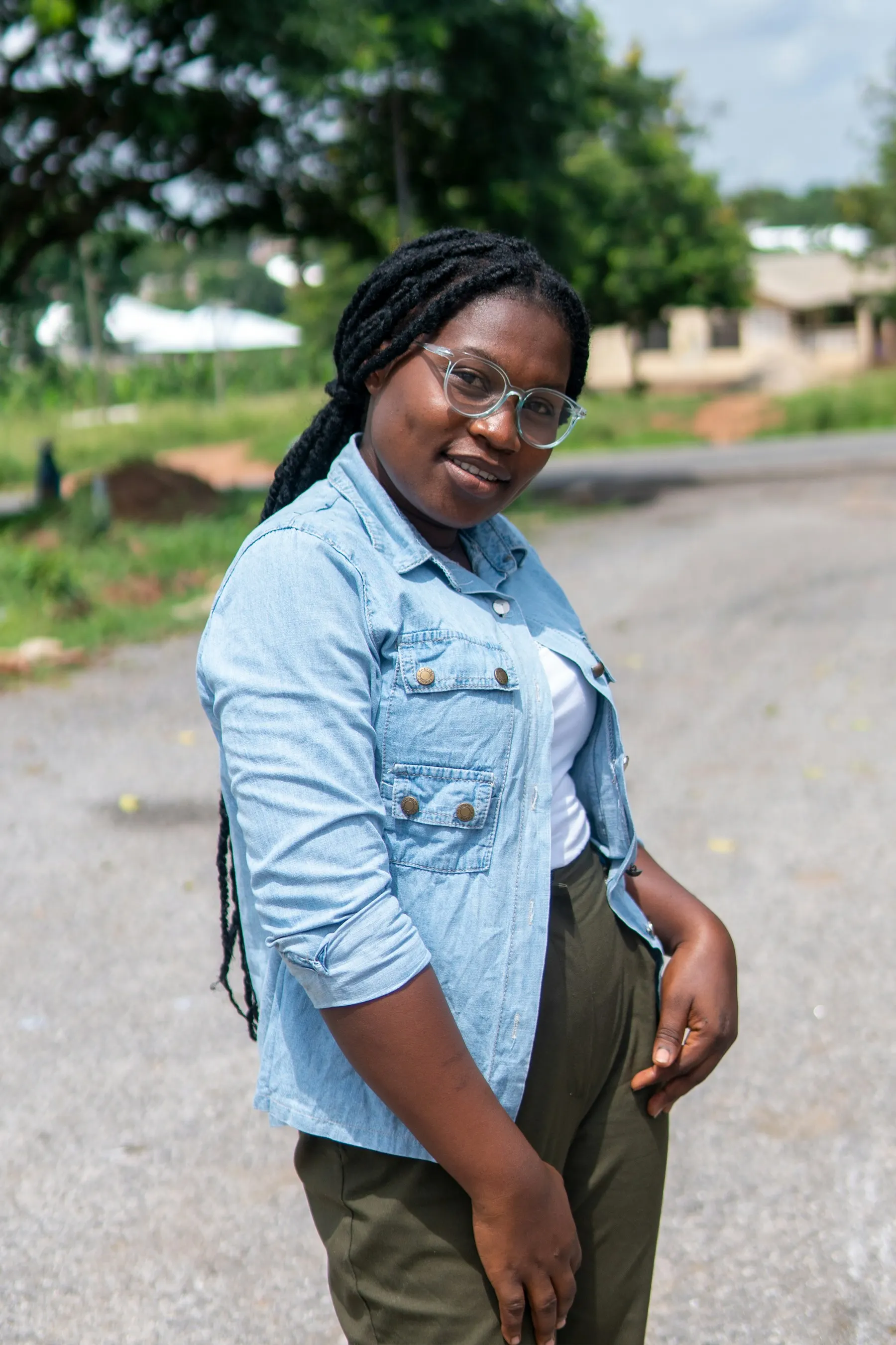 A smiling young woman in a denim shirt standing on a road
